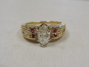 Marquise shaped diamond in a gold ring textured with accent diamonds and pink gemstones