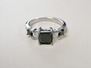 white gold ring with 5 gemstones. one large dark green square gemstone central with 2 diamonds and 2 smaller dark green gemstones