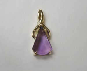 purple triangular gemstone set in a gold pendant