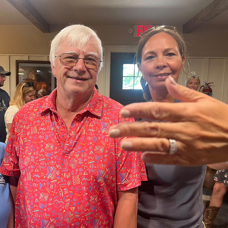 a woman standing next to a man with her hand in the foreground of the picture showing off a ring