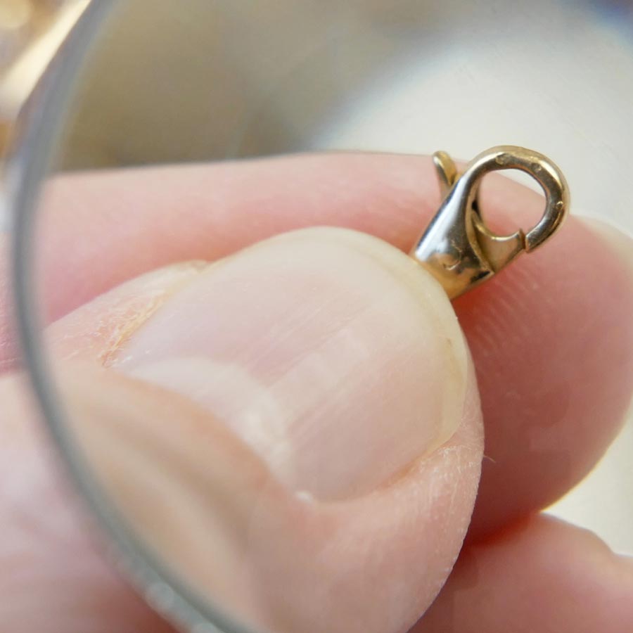closeup of jewelry clasp being held in the hand and viewed through a magnifying glass