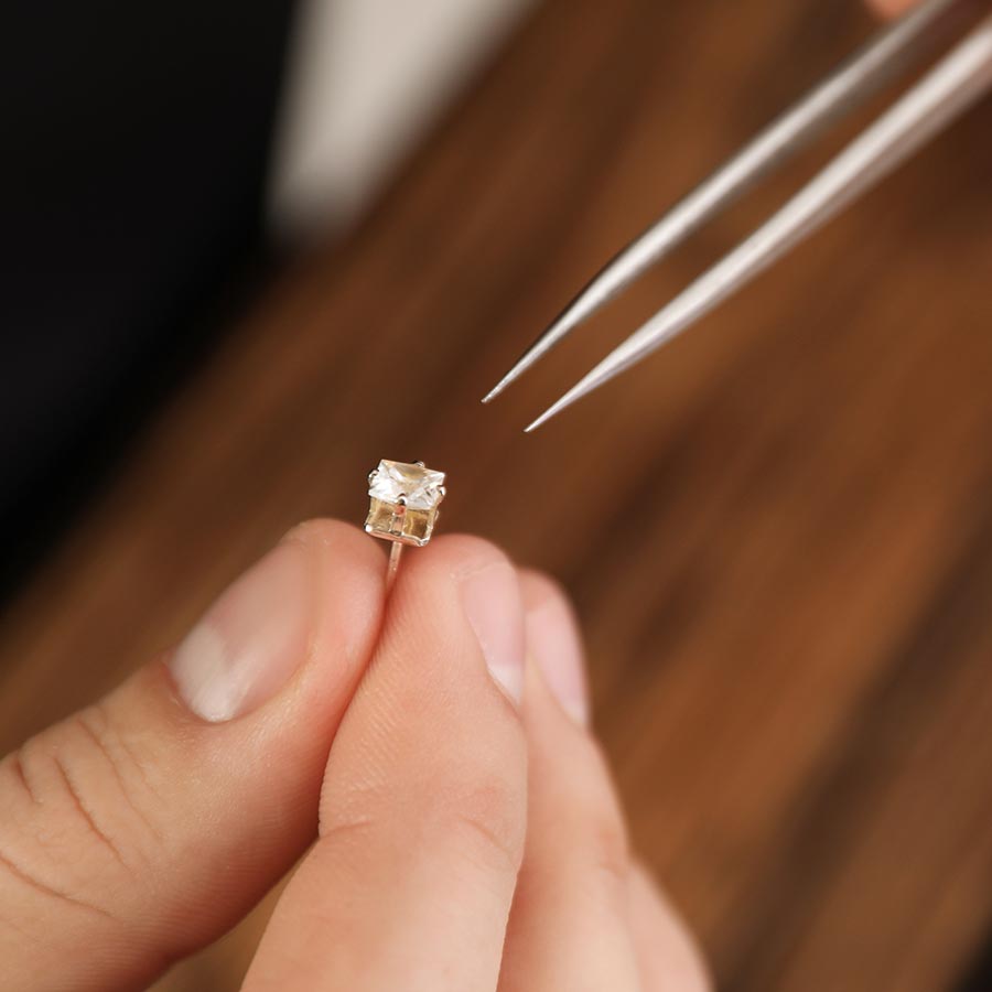 closeup of a jeweler's fingers holding a diamond stud earring about to be repaired with tweezers