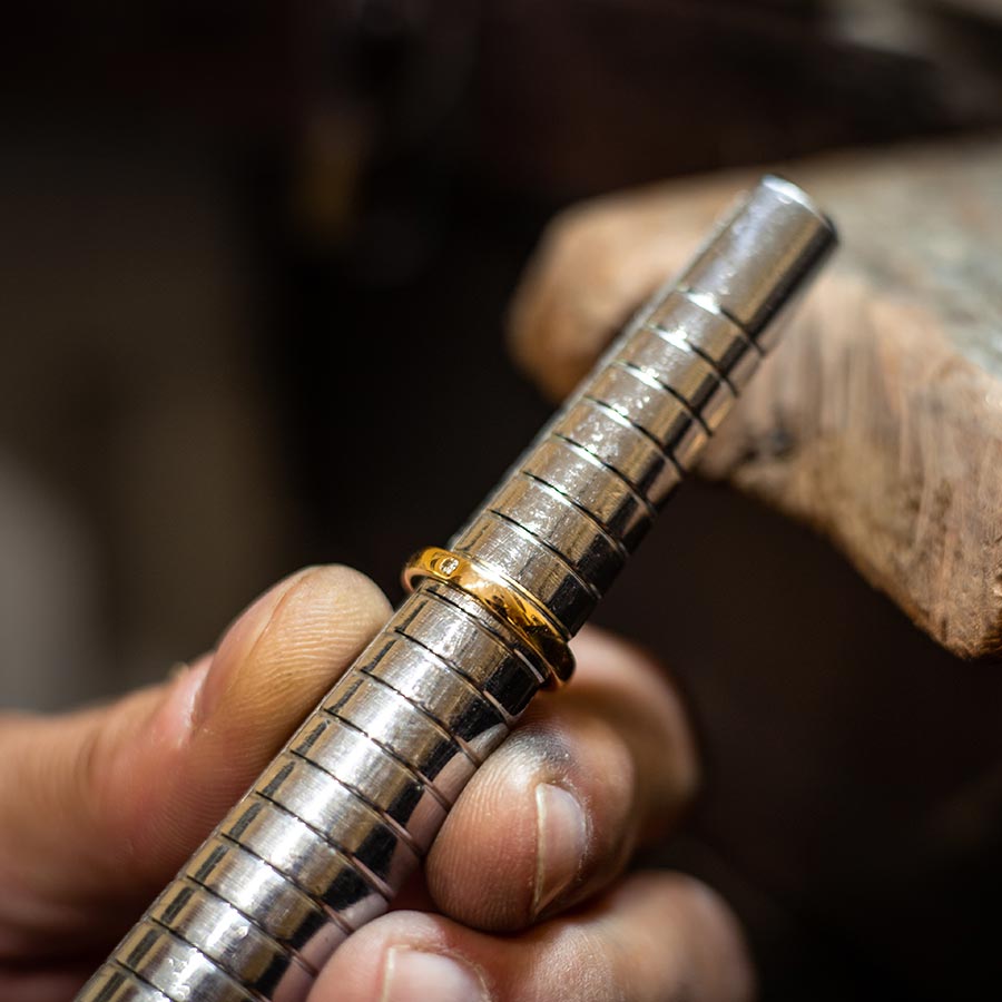 close up of a a gold band slid halfway down a ring sizing tool being held in a hand